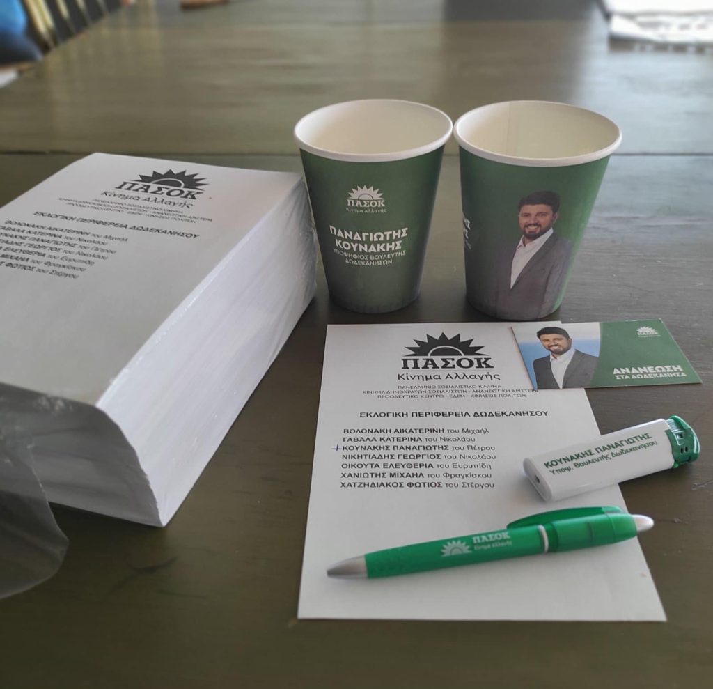 Υποψήφιος του ΠΑΣΟΚ στα Δωδεκάνησα μοιράζει ποτήρια του καφέ μίας χρήσης με φόντο τον πράσινο Ήλιο